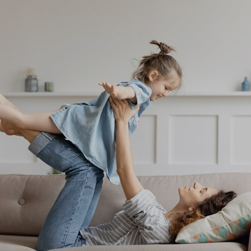 woman playing airplane with child on couch